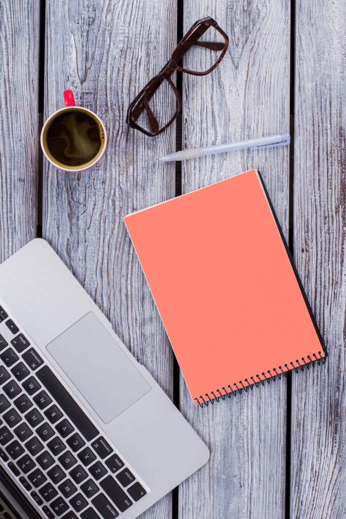 QWERTY notebook A notebook, laptop, pair of glasses, and a cup of coffee on a table and oh my god that coffee looks really good