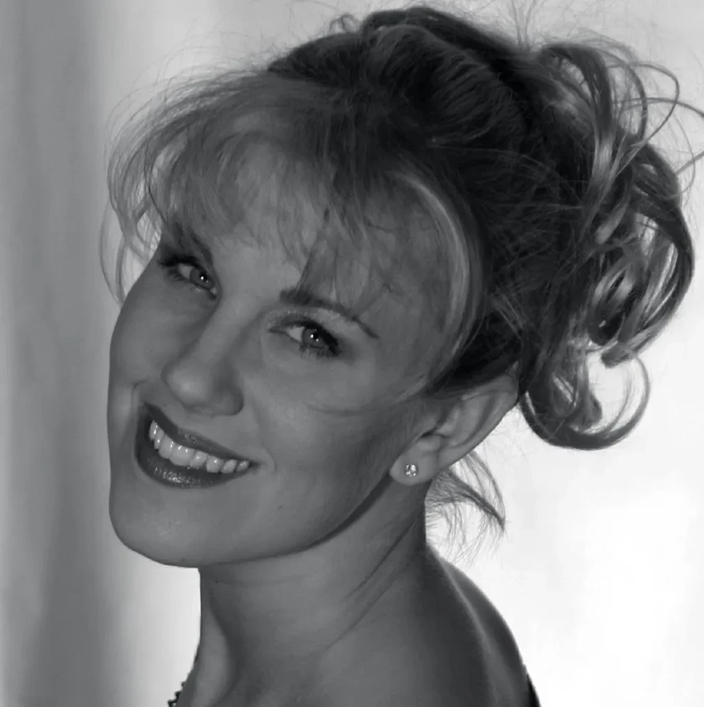 A black and white image of my friend Solinea, in her prime. She is blonde, with her curly hair up in a messy ponytail as she looks over her shoulder into the camera. She is stunning.