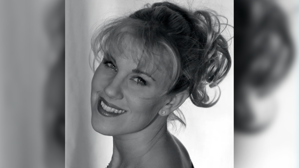 A black and white image of my friend Solinea, in her prime, looking over her shoulder. She is a blonde, with her hair up in a messy, curly ponytail, bangs framing her gorgeous face.